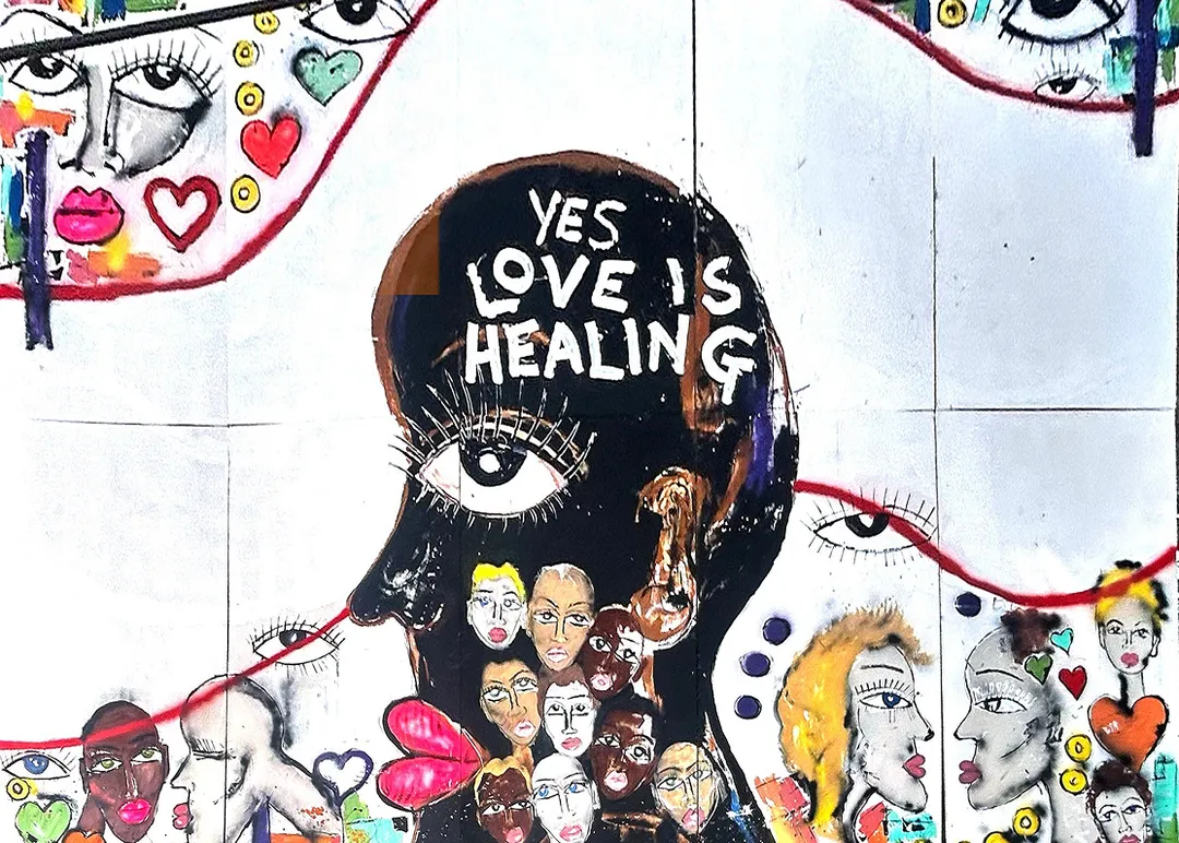 Bloom - close-up of Miles Regis mural featuring a central figure with 'Yes Love Is Healing' text and a crowd of painted faces