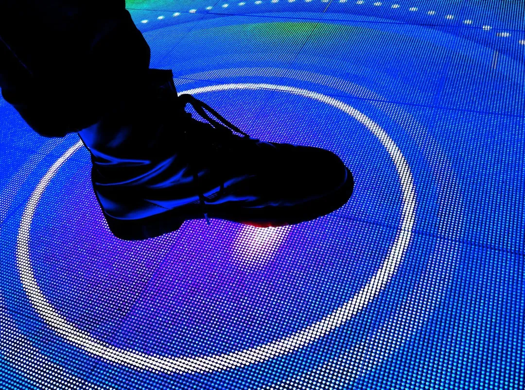 Close-up of a player's boot stepping into a glowing target ring on the Famous Footwork LED floor