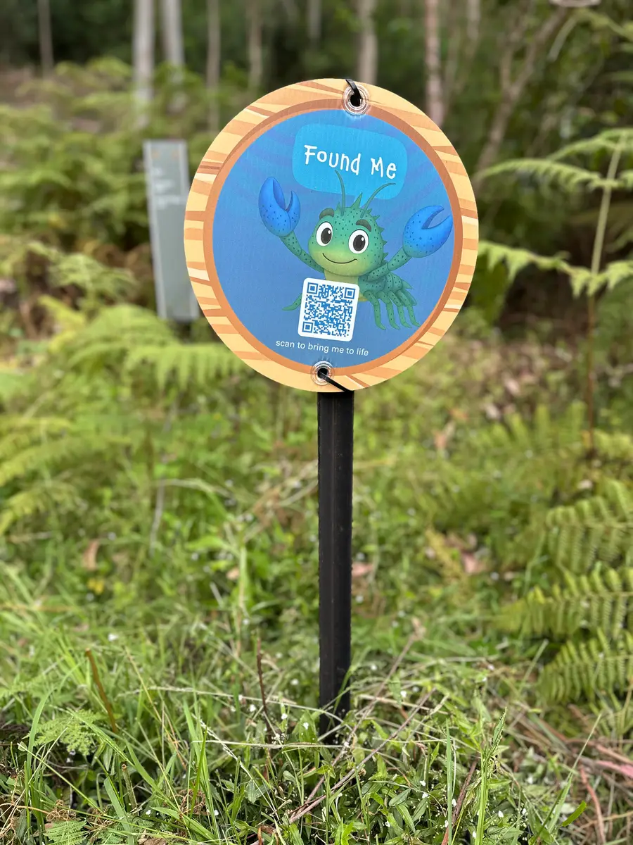 Hide and Go Creek - Found Me disc on a timber post in bracken beside the Waitara Creek trail, with a QR code that unlocks Craig in AR