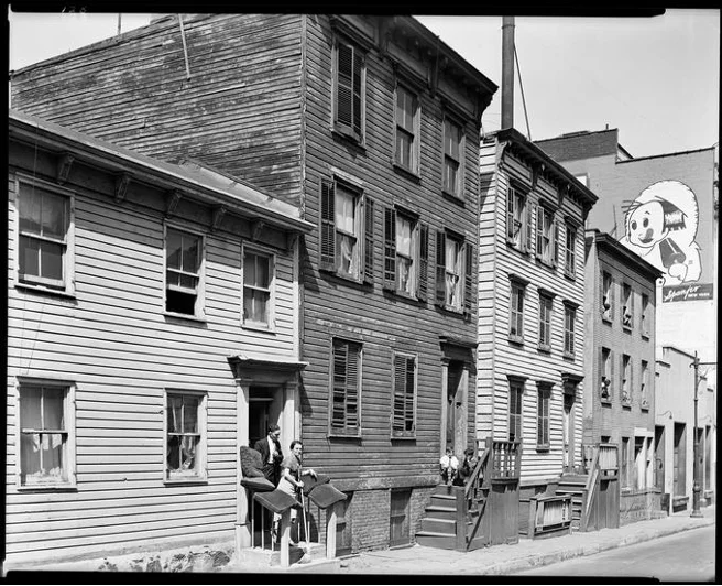 Archival black-and-white photograph of wooden clapboard row houses on a Brooklyn street