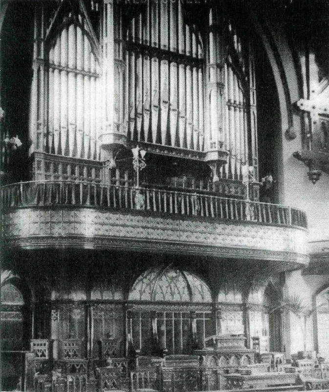 Historical black-and-white photograph of an ornate church pipe organ with carved woodwork balcony