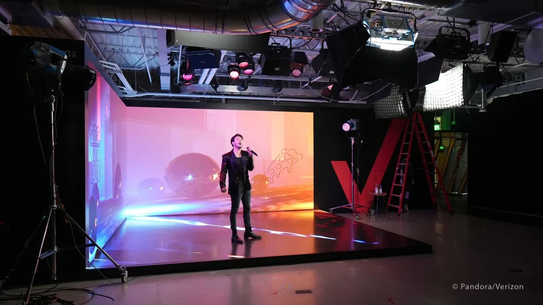 Sebastian Yatra singing on a physical LED stage, lit by an overhead rig, with the virtual environment displayed on the LED wall behind him